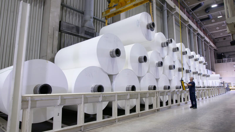 Standbild aus Ausstellungs-Video: Arbeiter manövriert große Papierrollen in Papierfabrik